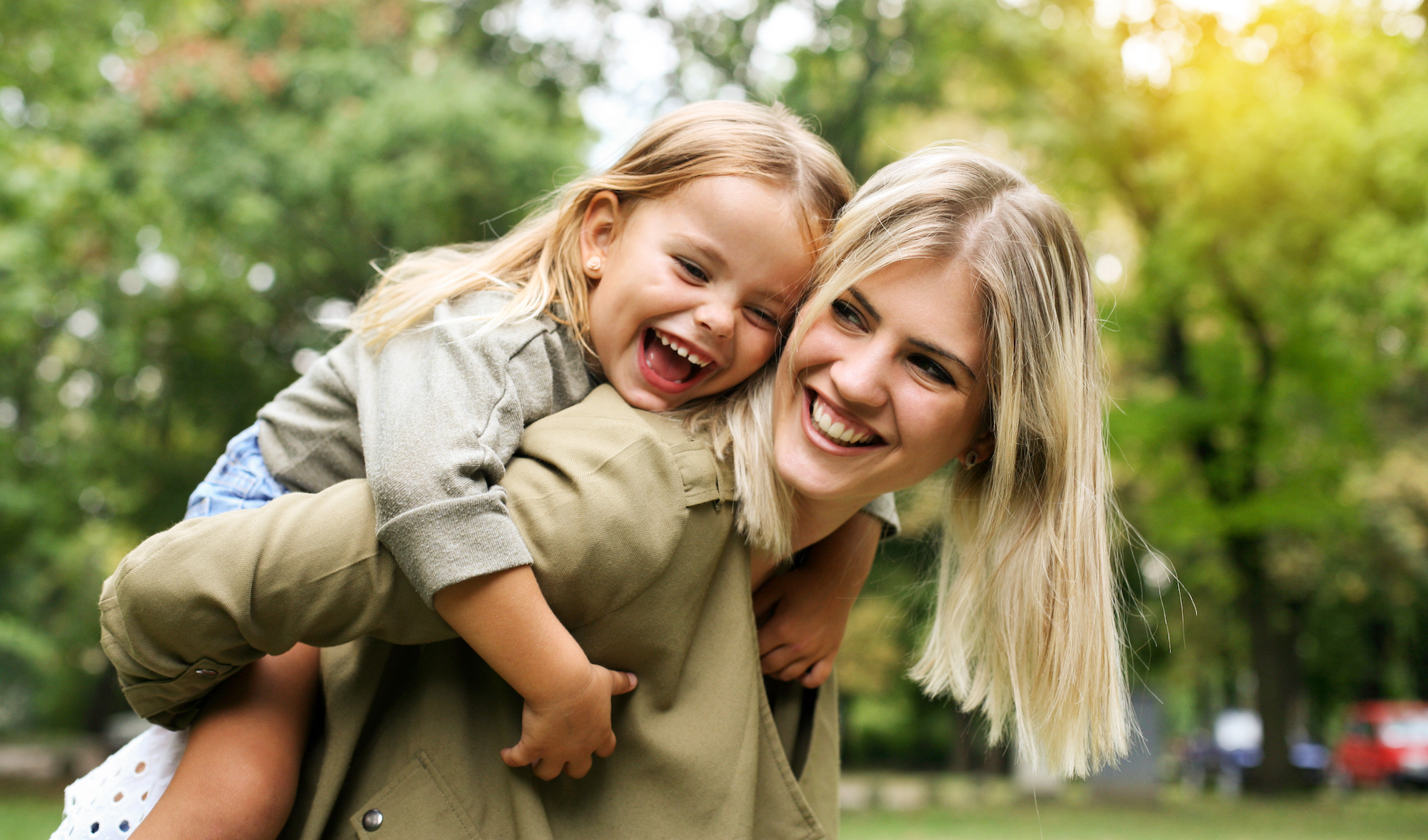 Young daughter outdoors on a piggy back ride with her mom